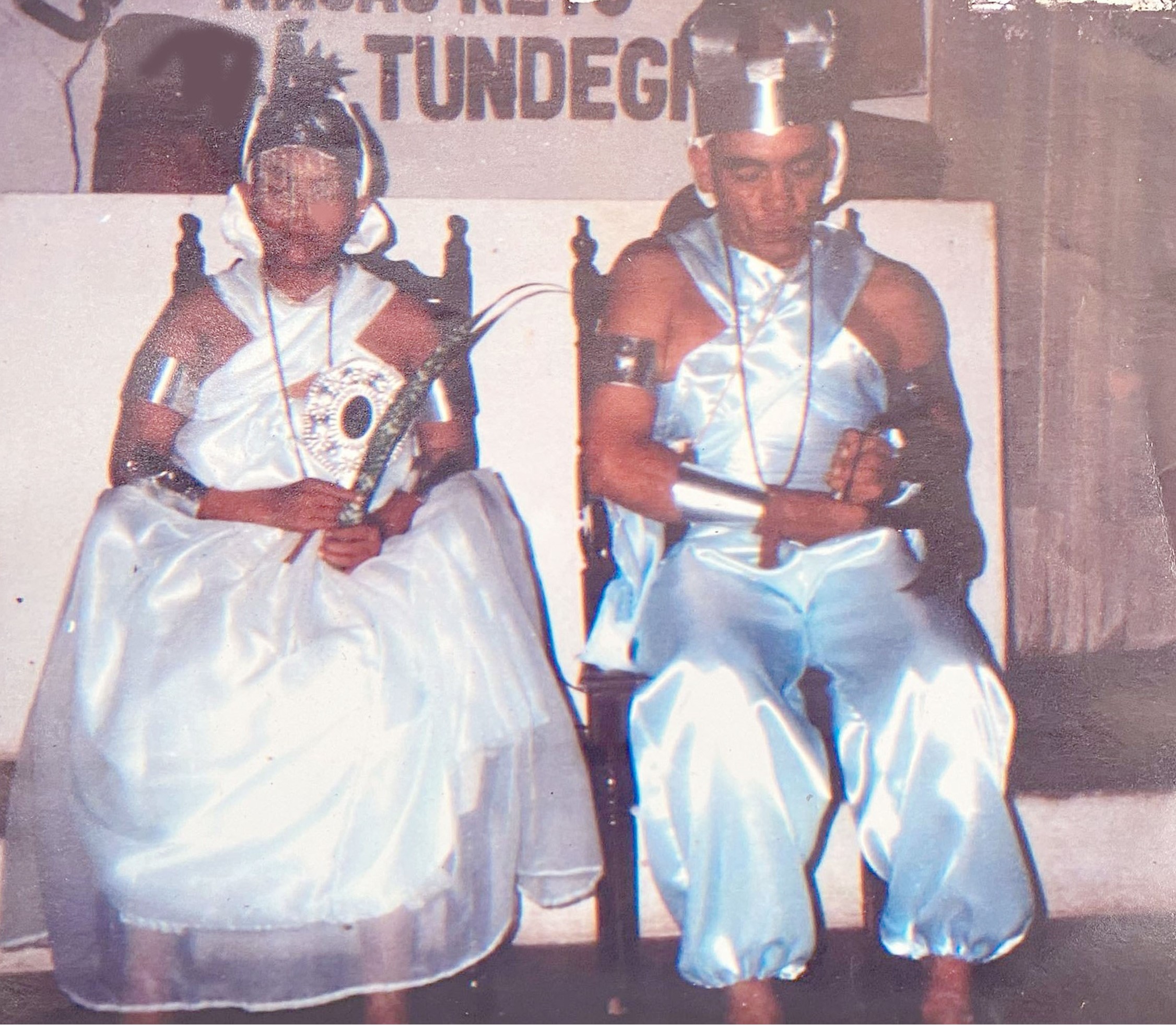 A imagem é uma fotografia antiga digitalizada, nela aparecem duas pessoas sentadas, centralizadas e que ocupam toda imagem. Elas estão vestidas com roupas de seus orixás, a esquerda a recém Yaô Anna filha de Iemanjá está vestida toda de branco, com adornos pratas e uma folha de espada de são Jorge e um espelho na mão. A Direita Seu Irmão de santo Francisco com uma roupa azul clarinha de cetim e adornos também prateados. Ambos se sentam em cadeiras de madeira, estão com olhos fechados. Ao fundo uma parede branca com alguns escritos que não é possível ler.